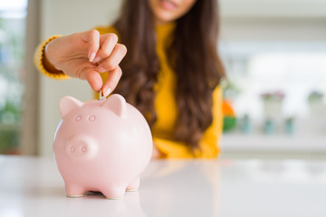 Close up of woman smiling putting a coin inside piggy bank as investment