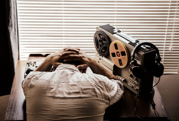 Tired special agent listens on the reel tape recorder. Officer wiretapping in headphones. Spying of...