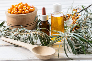 resh organic sea buckthorn oil with green branches of sea buckthorn on light wooden background. Alternative herbal medicine concept. Ingredients for natural cosmetics.