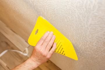 Man is using scraper to install wallpaper. Levelling of the wall. Maintenance repair works renovation in the flat. Restoration indoors.