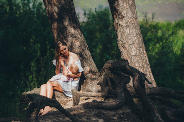 Mother breastfeeding her baby on a sunny day in shadow of old big tree