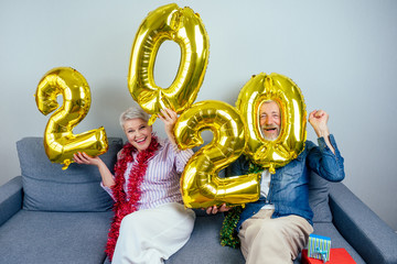 Happy beautiful elderly couple wearing christmas tinsel on neck celebrating new year at home in...