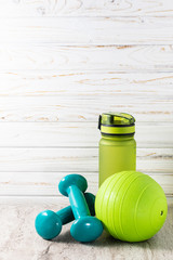 Sport equipment on light background with copy space for your design. Healthy lifestyle and fitness concept. Dumbbells,  ball and water bottle on light wooden background. - obrazy, fototapety, plakaty