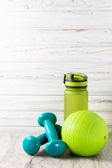 Gardinen Sport equipment on light background with copy space for your design. Healthy lifestyle and fitness concept. Dumbbells,  ball and water bottle on light wooden background. © Iryna