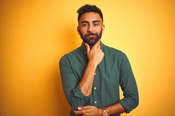 Young indian businessman wearing elegant shirt standing over isolated white background looking confident at the camera with smile with crossed arms and hand raised on chin. Thinking positive.