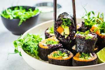 Vegan sushi rolls with black rice, avocado and sweet potato on white dish. Vegan food concept.