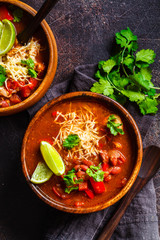 Traditional mexican bean soup with meat and cheese in wooden bowl, dark background. Mexican food concept.