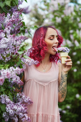 Fashion girl with bright red dyed hair in Apple and lilac flowers. Creative color bright pink,...