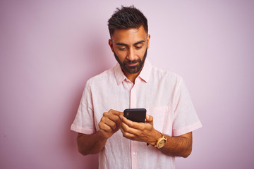 Young indian man using smartphone standing over isolated pink background with a confident expression on smart face thinking serious
