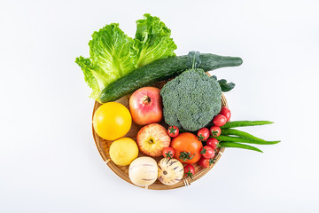 A bamboo plate filled with fresh seasonal vegetables and fruits on a white background