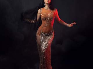The body of a beautiful girl in a bead costume for belly dance on a black background of a stormy sky. Sexy dramatic woman dancing oriental dance in the light of red spotlights.