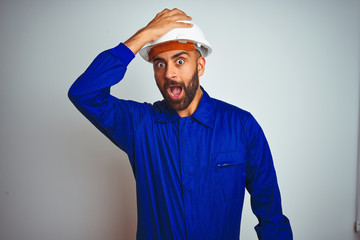 Handsome indian worker man wearing uniform and helmet over isolated white background surprised with...