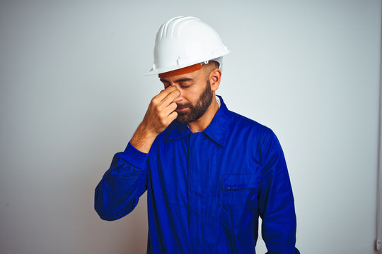 Handsome indian worker man wearing uniform and helmet over isolated white background tired rubbing nose and eyes feeling fatigue and headache. Stress and frustration concept.