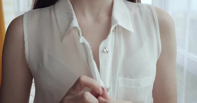 Unrecognizable woman unbuttoning white blouse at home.