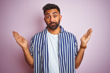 Young handsome indian man wearing summer striped shirt over isolated pink background clueless and...