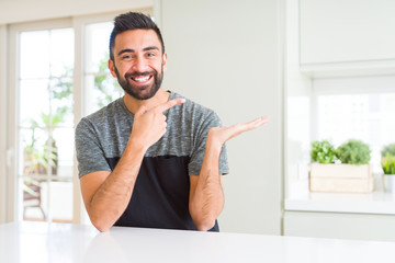 Fototapeta premium Handsome hispanic man wearing casual t-shirt at home amazed and smiling to the camera while presenting with hand and pointing with finger.