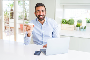 Fototapeta na wymiar Handsome hispanic man working using computer laptop and drinking a cup of coffee with a happy face standing and smiling with a confident smile showing teeth