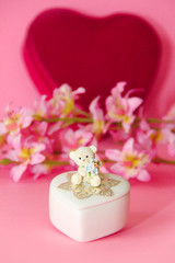 ceramic white casket with a teddy bear on a background of pink flowers and hearts
