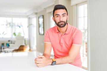 Fototapeta premium Handsome hispanic man wearing casual t-shirt at home with serious expression on face. Simple and natural looking at the camera.