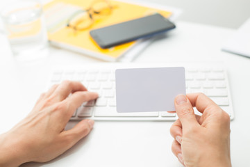 Blank white credit card mockup in hand on keyboard background. 