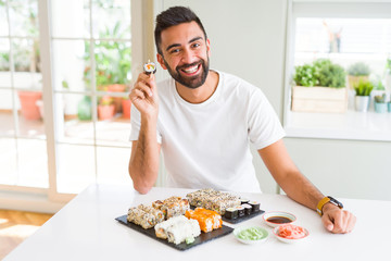 Handsome man smiling happy enjoying eating fresh colorful asian sushi using chopsticks
