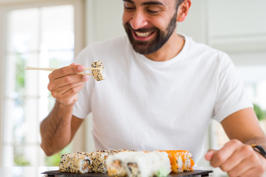 Handsome man smiling happy enjoying eating fresh colorful asian sushi using chopsticks