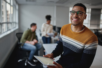 Portrait of a confident male entrepreneur with digital tablet smiling to camera in a working environment