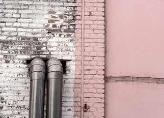 The part of the wall, painted in white and pink, from which two pipes stick out. Background, texture.