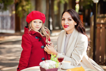 Smiling mom helps little cute daughter fasten her red coat.