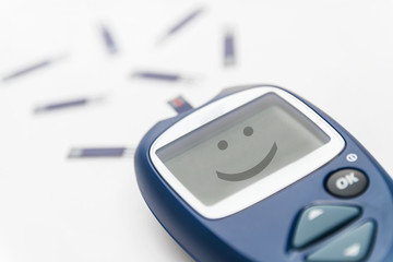 Glucometer with test strip with smile on the monitor. Blood glucose meter with a lot of test strips on the background. Closeup, selective focus