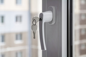 Handle with lock and key on the PVC window. Apartment house on the background. Closeup, selective...