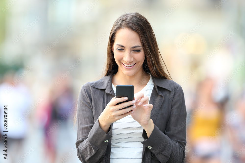 Sticker Front view of happy woman using smart phone in the street