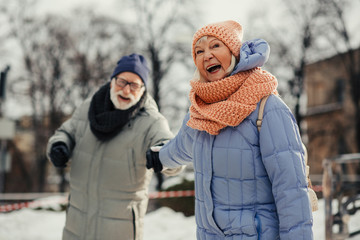 Excited aged woman pulling hand of her husband and smiling