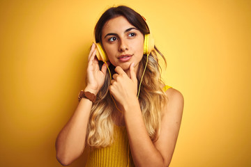 Young beautiful woman wearing headphones over yellow isolated background serious face thinking about question, very confused idea