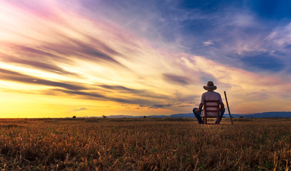 farmer sitting on a chair looking at the field and sunset - obrazy, fototapety, plakaty