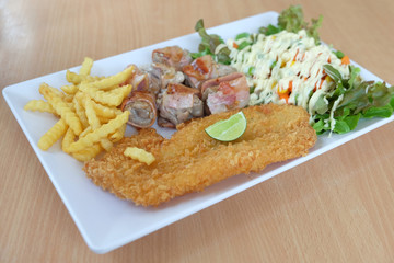 Fried fish, bacon roll, french fries, vegetable salad in white plate