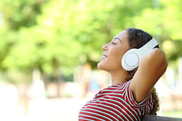 Happy mixed race woman listening to music resting in a park