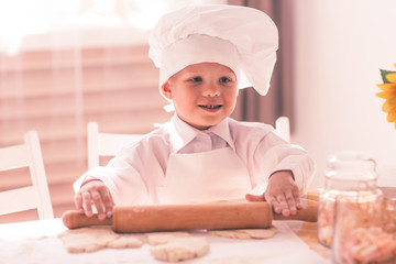 little baby in a cook rolls out the dough with rolling pin and smiling