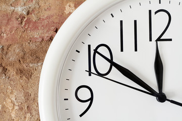 Lunch time concept. A part of white round analog clock face against the background of a red brick wall is showing lunch time.