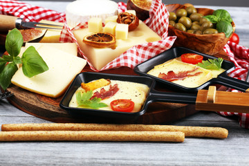 Fototapeta na wymiar Delicious traditional Swiss melted raclette cheese on diced boiled or baked potato and baguette served in individual skillets with salami..