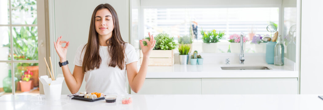 Wide angle picture of beautiful young woman eating asian sushi from delivery relax and smiling with eyes closed doing meditation gesture with fingers. Yoga concept.