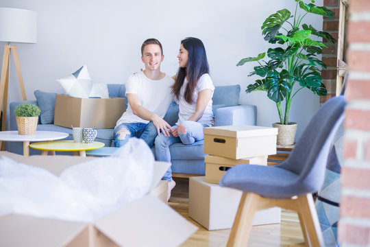 Young beautiful couple sitting on the sofa drinking coffee at new home around cardboard boxes