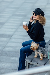 Young beautiful woman with Yorkshire Terrier, against green of summer city have a break time.