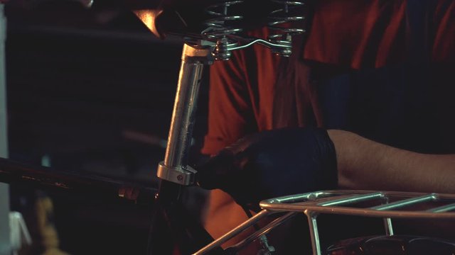 theme small business bike repair. A young Caucasian brunette man wearing safety goggles, gloves and an apron uses a hand tool to repair and adjust the bike in the workshop garage