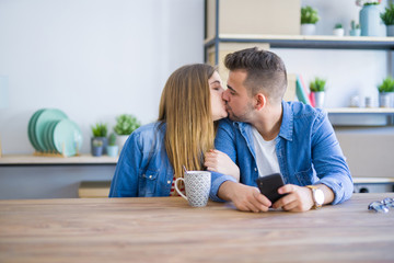 Young couple relaxing drinking a cup of coffee and using smartphone, sitting at new home with cardboard boxes behind them