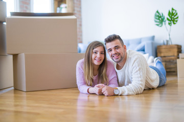 Young beautiful couple in love moving to new home, lying on the floor around cardboard boxes, very happy and cheerful for new apartment