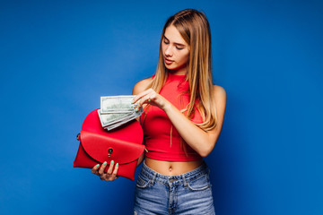Pretty young girl in a checkered blouse holds one hundred dollars bills and wallet on blue...