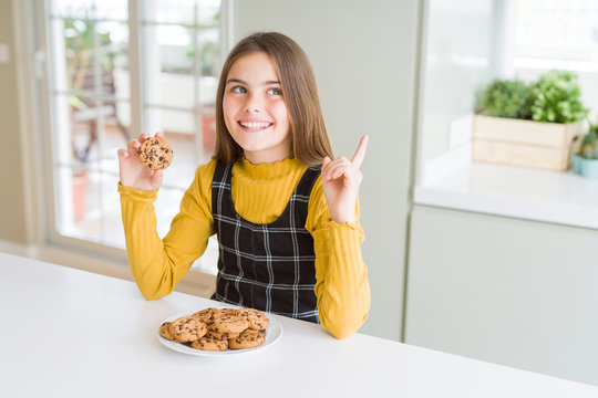 Beautiful young girl kid eating chocolate chips cookies very happy pointing with hand and finger to the side