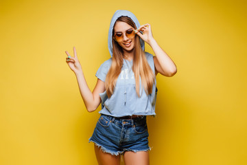 Young blonde, cute  woman over isolated yellow wall in sunglasses  posing.