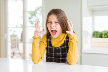 Young beautiful blonde kid girl wearing casual yellow sweater at home crazy and mad shouting and yelling with aggressive expression and arms raised. Frustration concept.